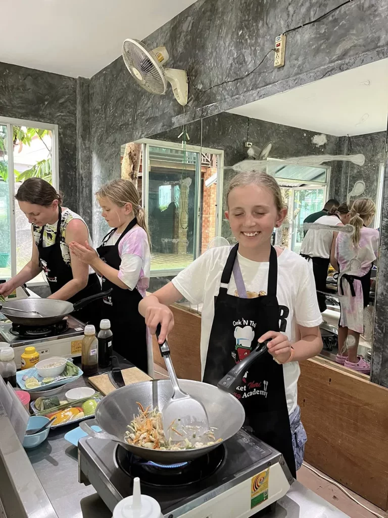 Phuket Family Trip: A young girl happily learning to cook Thai food during a family cooking class in Phuket