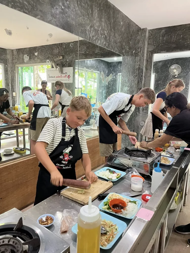 Phuket Family Trip: Kids learning to cook authentic Thai dishes during a hands-on cooking class in Phuket, chopping vegetables and preparing local recipes together.