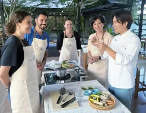 Students enjoying a hands-on Phuket Thai cooking class in a tropical garden setting