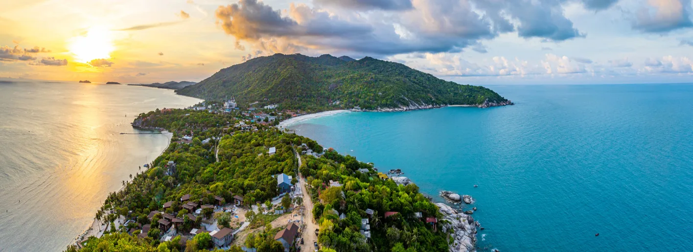 Stunning aerial view of Koh Samui at sunset, showing the lush green island surrounded by turquoise waters, with a golden sun setting over the horizon and scattered clouds in the dramatic sky.