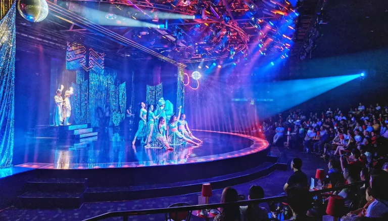 Cultural Show and Cabaret Show in Thailand: Indoor cabaret show at Calypso Bangkok with performers in sequined costumes on a curved stage, disco ball overhead, and audience seated at tables