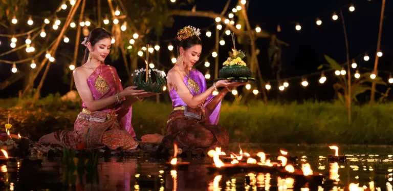 Loy Krathong Festival: Women in silk Thai costumes release decorated krathongs with candles on water during Loy Krathong celebration