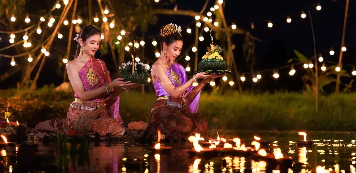 Loy Krathong Festival: Women in silk Thai costumes release decorated krathongs with candles on water during Loy Krathong celebration