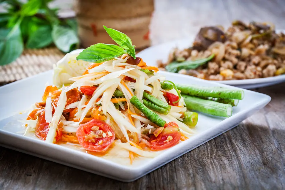 Thai food: Som Tum Thai papaya salad with tomatoes, green beans, and fresh herbs on a white plate