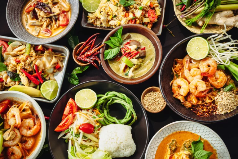 Thai food: Traditional Thai feast with multiple dishes including green curry, pad thai, fried rice, grilled shrimp, and som tam salad arranged on a wooden table