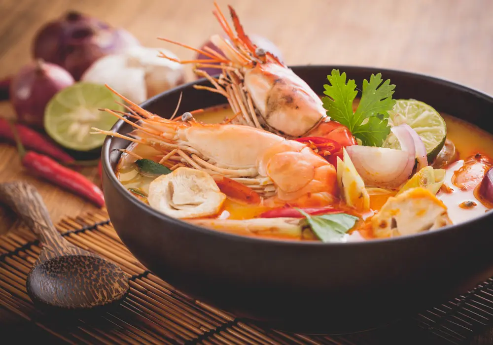 Thai food: Authentic Tom Yum Goong featuring fresh prawns, mushrooms, and Thai herbs in spicy clear broth, garnished with lime and cilantro