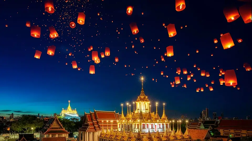 Sky lanterns floating above illuminated Bangkok temples during Loy Krathong festival at dusk