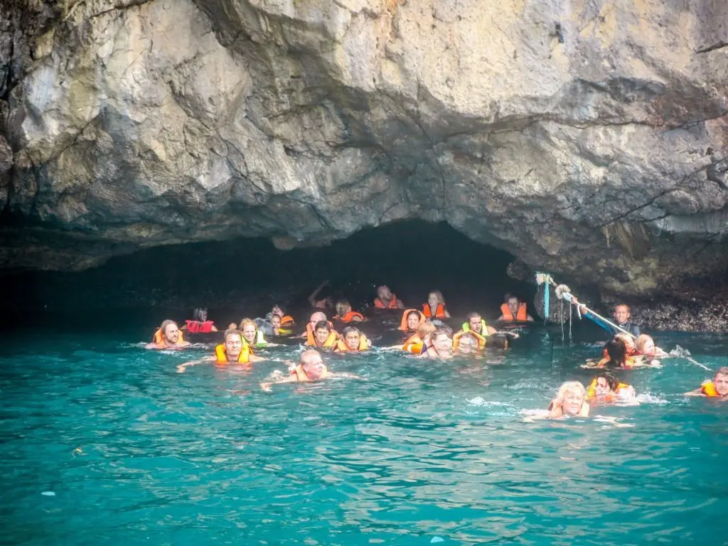 Hidden Thailand: Swimmers in life jackets navigating the bright turquoise waters beneath limestone cliffs in Emerald Cave