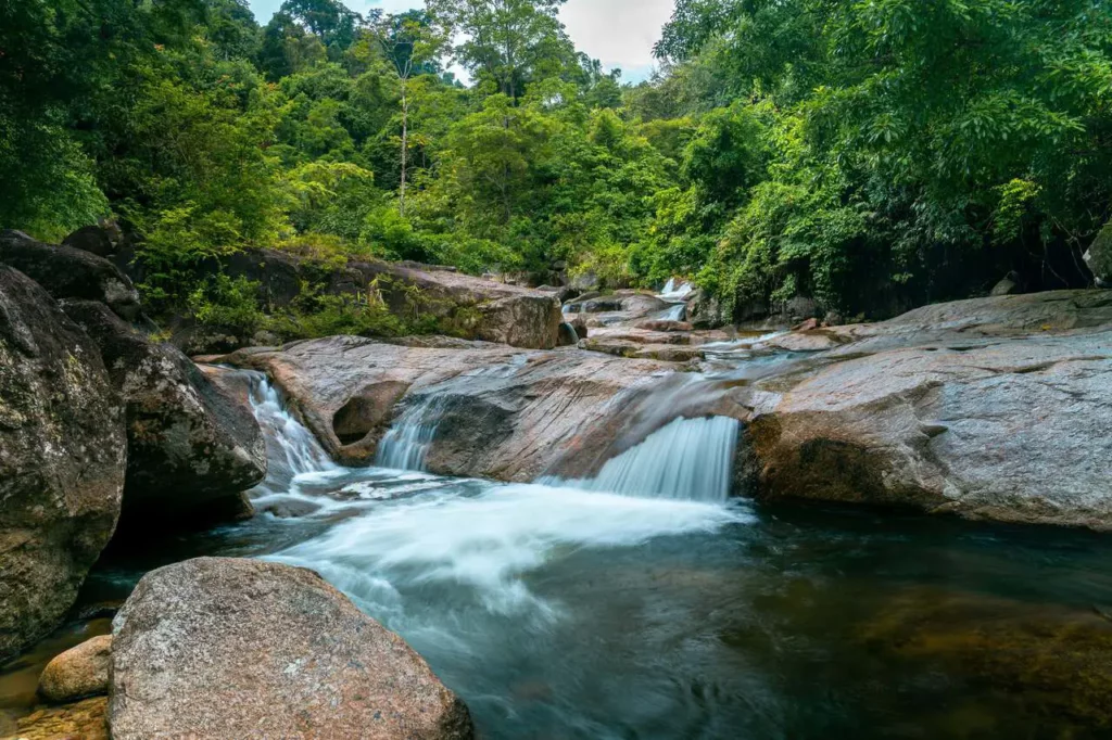 Hidden Thailand: Water cascading over smooth rock formations into a tranquil pool in Nakhon Si Thammarat's jungle