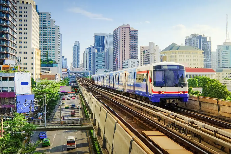 BTS Skytrain on elevated tracks in Bangkok with city buildings and traffic below aligns with budget travel Thailand plan.